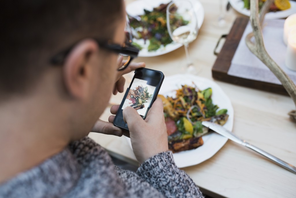 Man photographing plate of food at restaurant table
